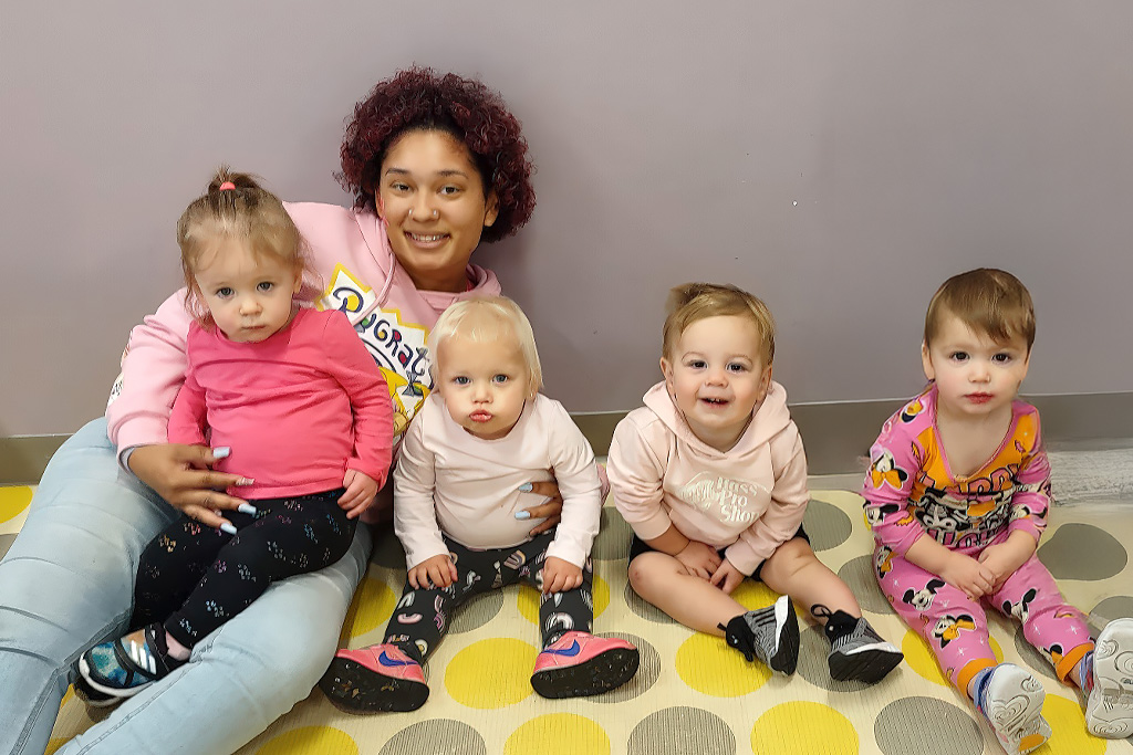 teacher and four toddlers seated on the floor, sharing a moment of togetherness.
